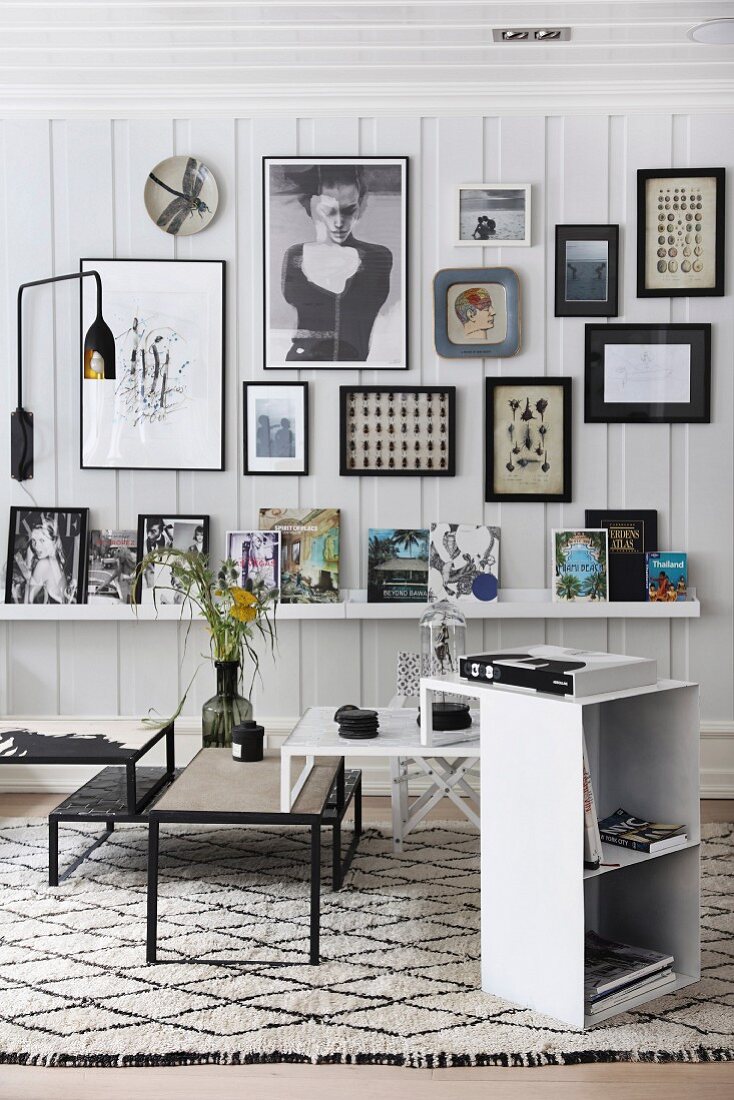 Set of coffee tables and small shelving unit on black and white patterned rug with collection of pictures on white wooden wall in background