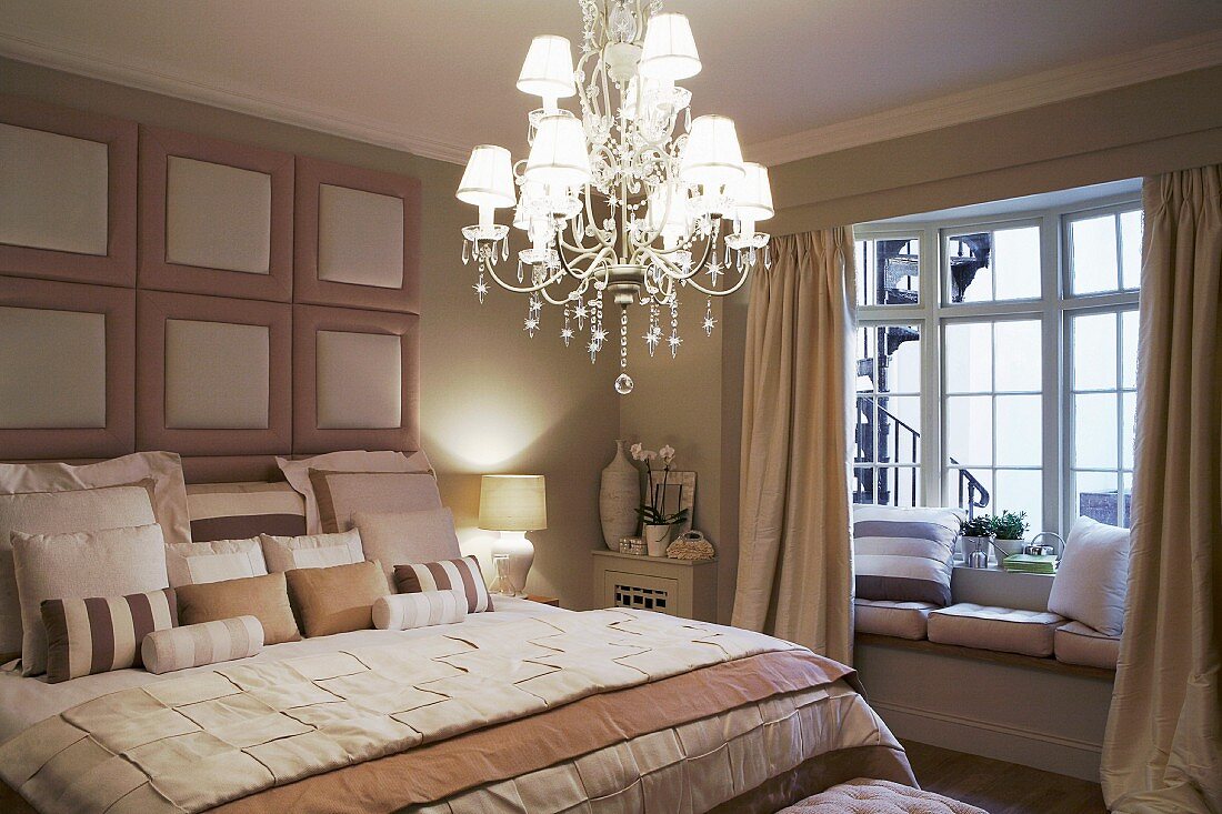 Elegant bedroom in subdued shades of beige with illuminated chandelier and window seat in bay window