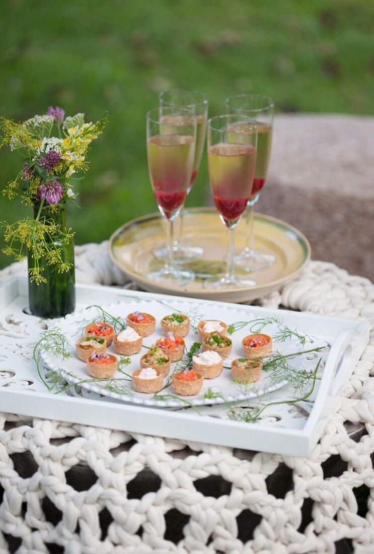 Dish of various canapés and Champagne cocktails in stemmed glasses on garden table