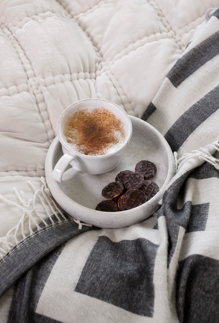 Eine Tasse Cappuccino und Kekse auf einem Marmortablett auf dem Bett