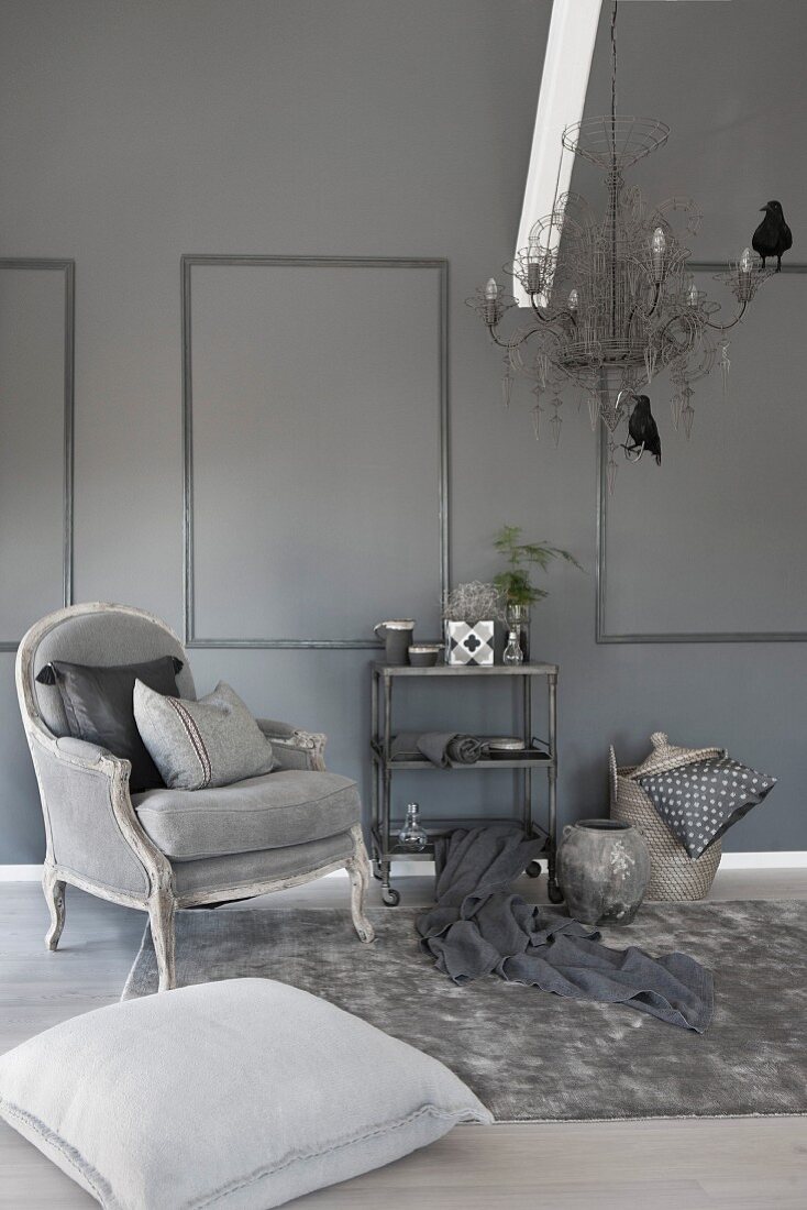 Stylish living room in shades of grey with antique armchair, fur rug and metal chandelier with bird ornaments