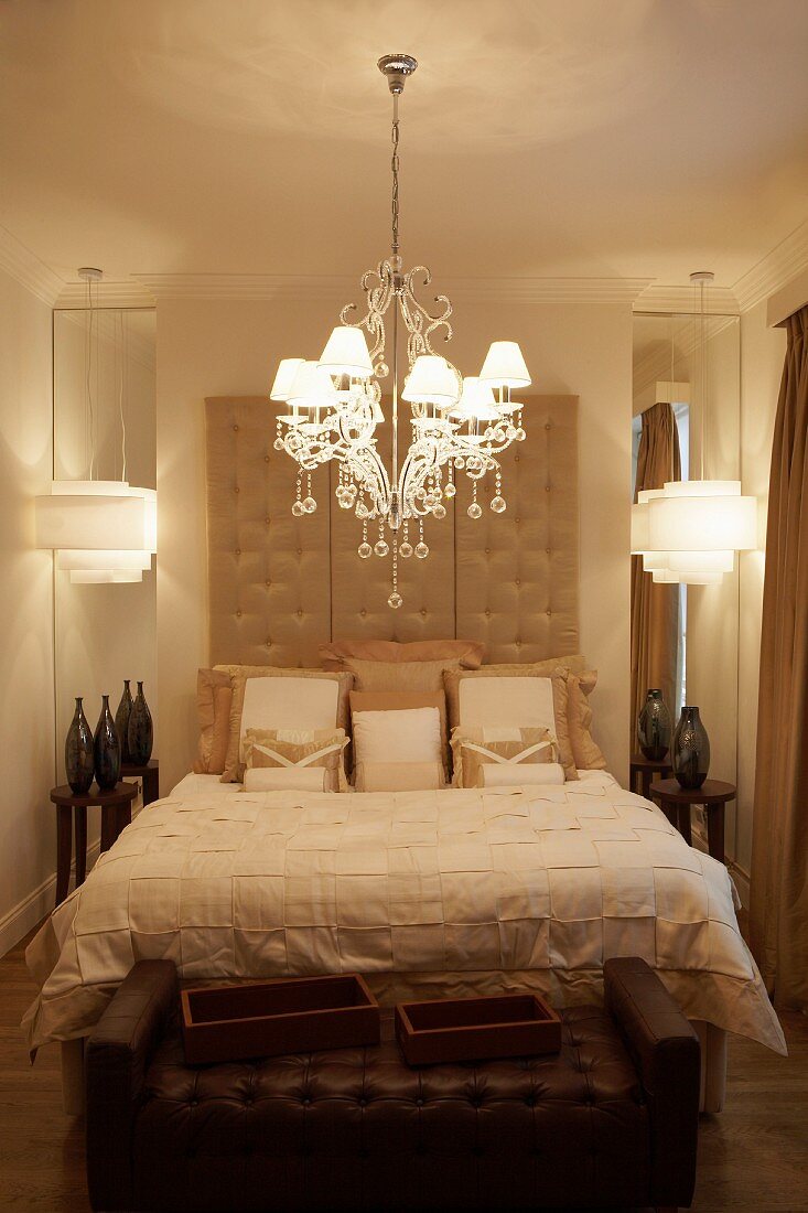 Kristallleuchter mit Lampenschirmchen über elegantem Doppelbett, gepolstertes Bettkopfteil und Vasen vor Wandspiegeln