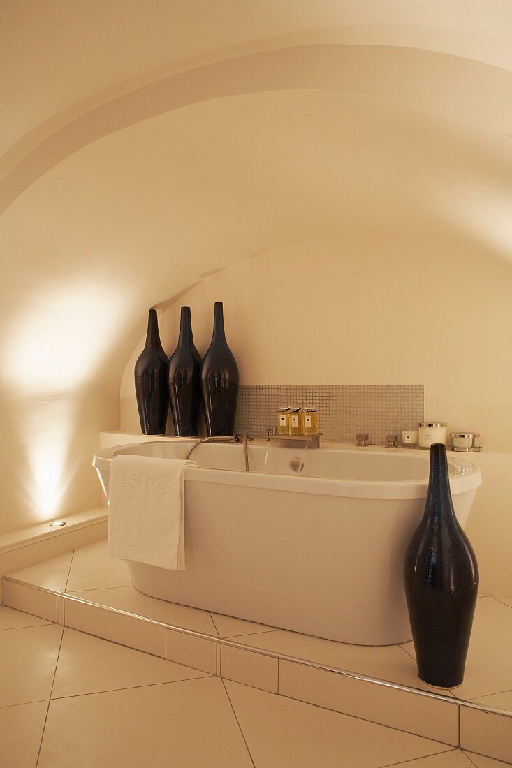 Free-standing bathtub on tiled platform in vaulted niche decorated with artistic vases shaped like bottles