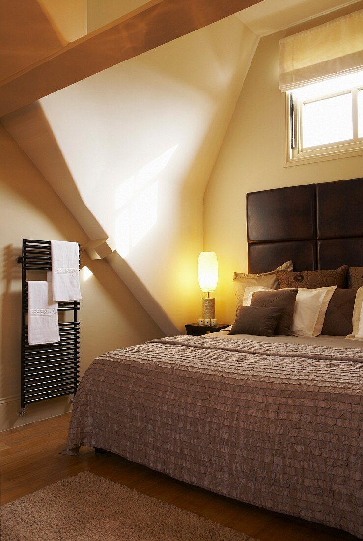 Doppelbett mit Kopfteil unter einer Dachnische mit Fenster, seitlich ein Handtuchheizkörper