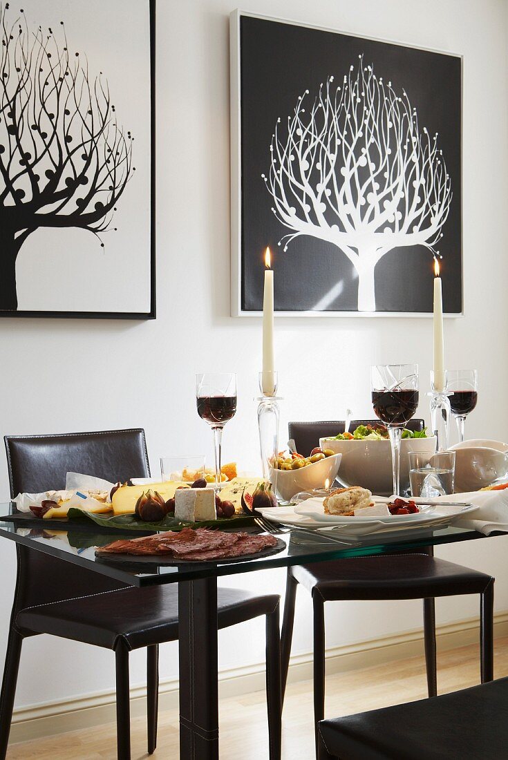 Festively set glass table, black leather chairs and graphical pictures of stylised trees