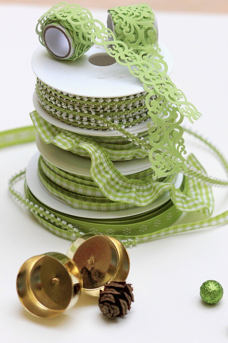 Gestapelte, hellgrüne Geschenkbänder und goldglänzende Kerzenhalter für Adventskranz