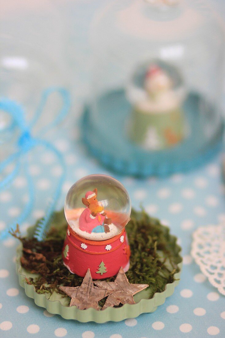 Vintage-style arrangement of snow globe on moss in pale green flan tin
