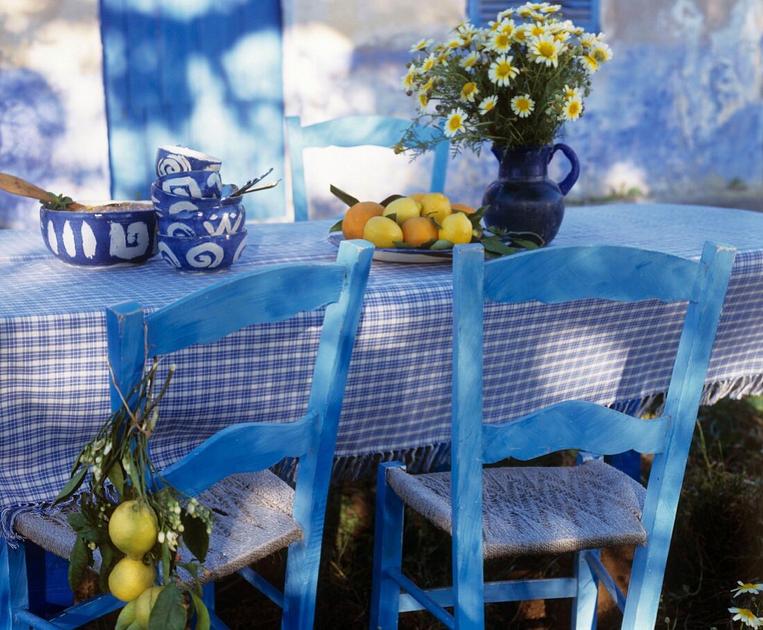 Blau lasierte Holzstühle vor Tisch mit weiss-blau karierter Tischdecke, in mediterranem Stil