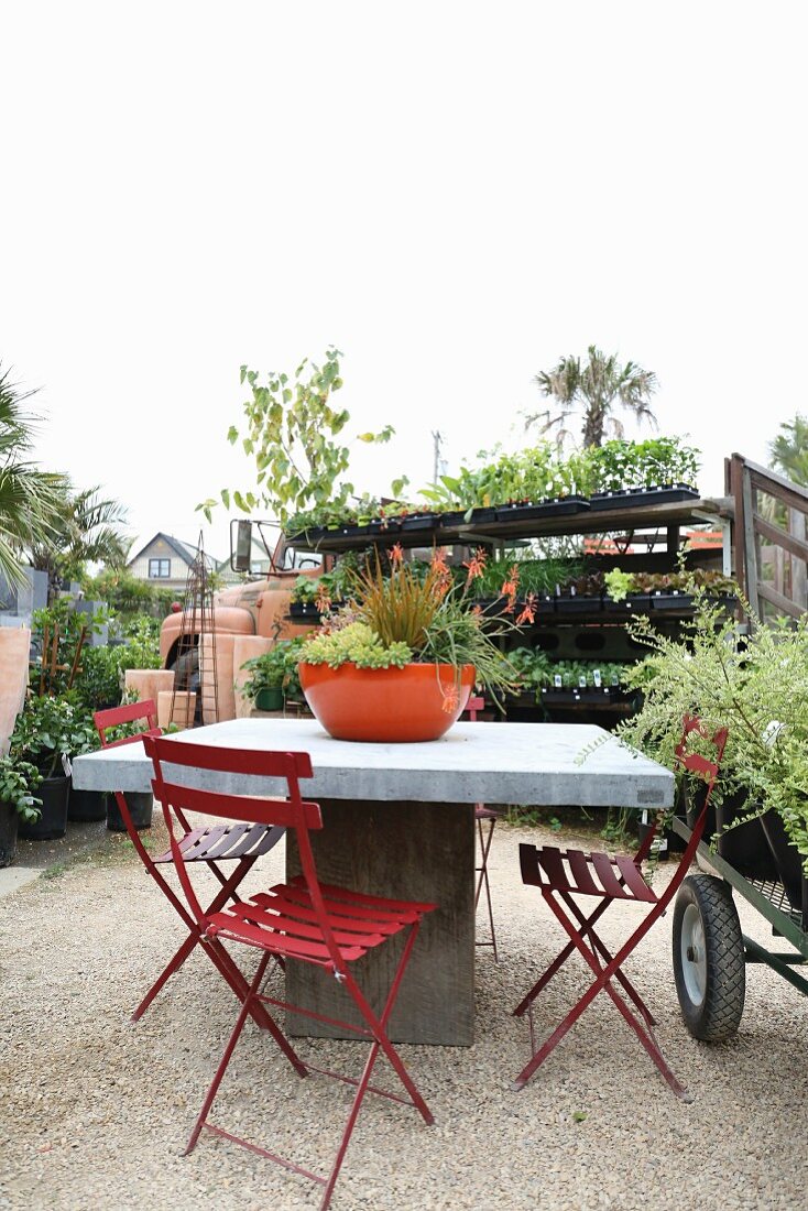 Table and red folding chairs on gravel floor in a garden center