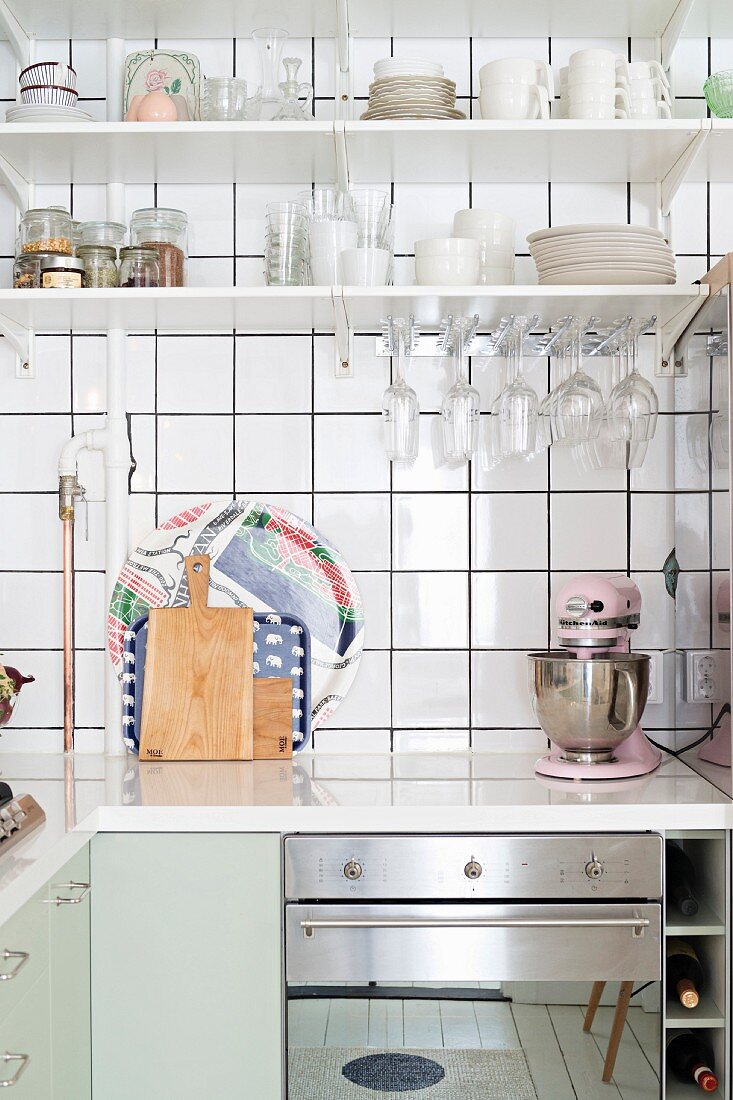 Küchenzeile übereck mit weisser Arbeitsplatte, darüber Regale mit Geschirr vor weisser Fliesenwand
