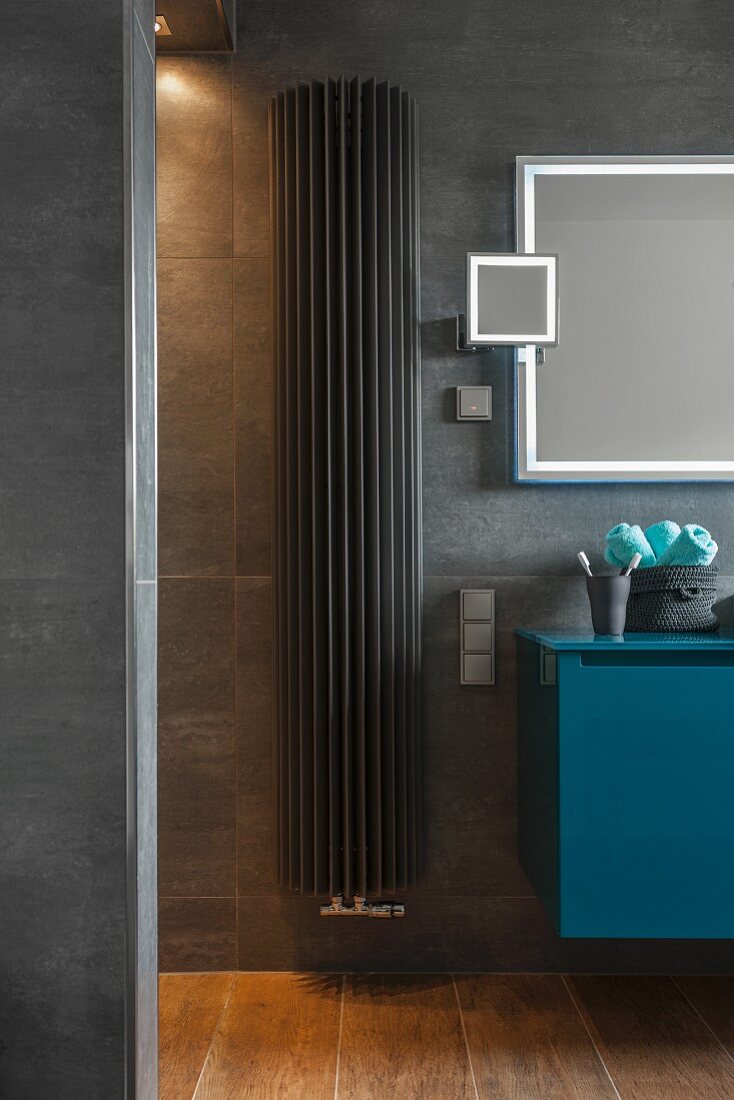 A dark grey heater between a shower and a petrol-blue washstand
