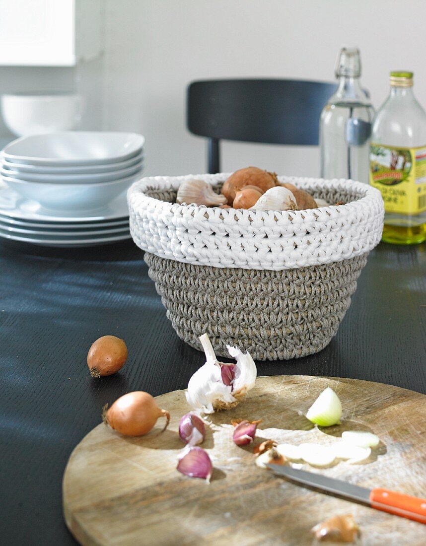A crocheted onion basket with a wooden chopping board in the foreground