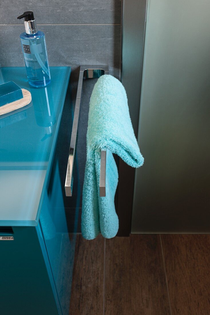 A turquoise towel on a stainless steel towel rail next to a washstand in a modern bathroom