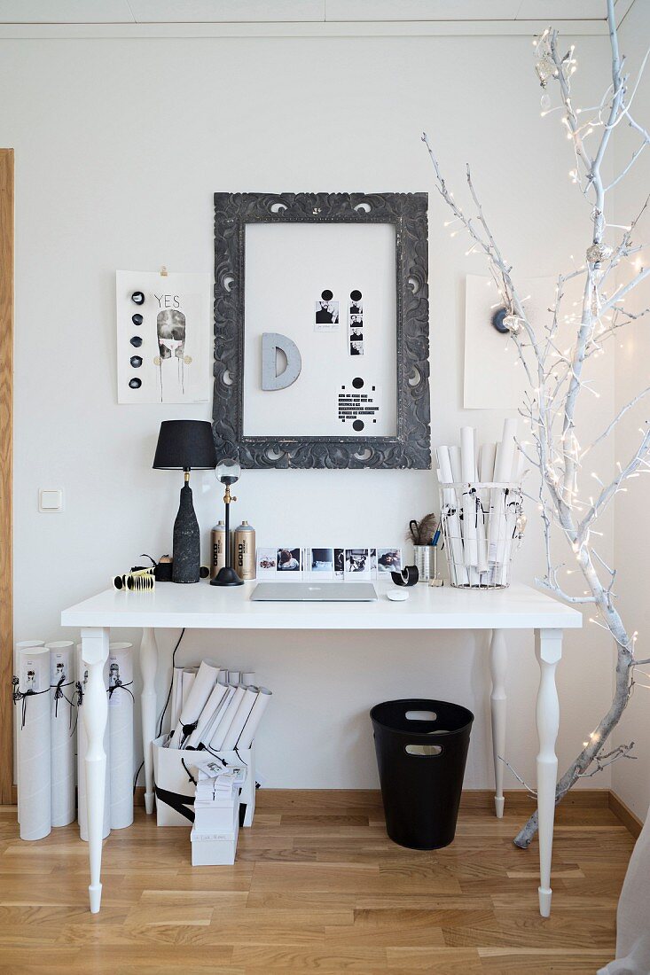 Fairy lights on white-painted branch next to white desk with black accessories