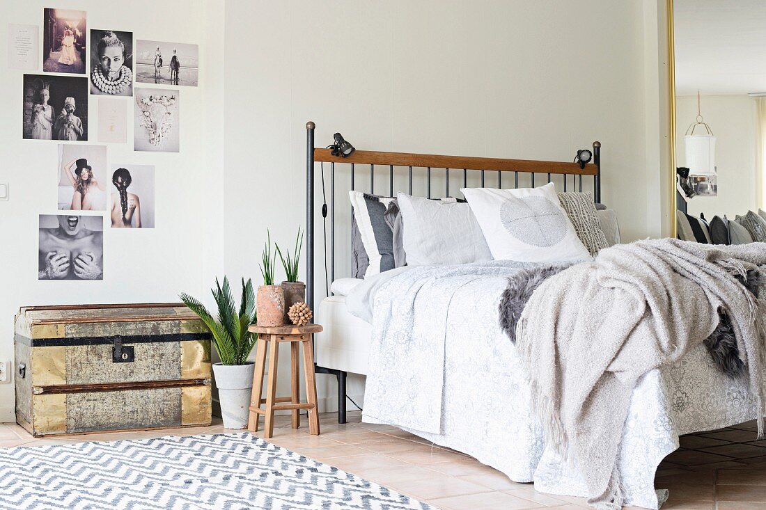 Bett mit vielen Decken und Kissen, daneben eine Truhe und Bildercollage