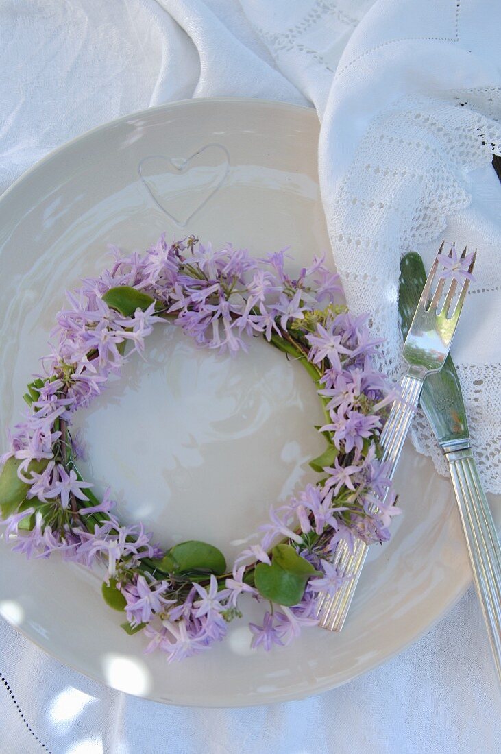 Blumenkranz mit violetten Blüten auf weißem Teller und Besteck