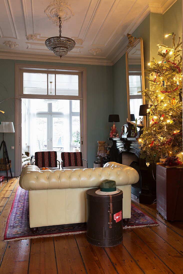 Beleuchteter Weihnachtsbaum im Wohnzimmer mit Stuckdecke und Chesterfieldsofa