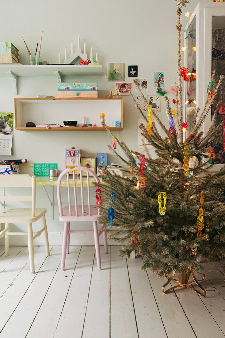 Geschmückter Weihnachtsbaum neben Schreibtisch mit Holzstühlen, oberhalb Wandregal