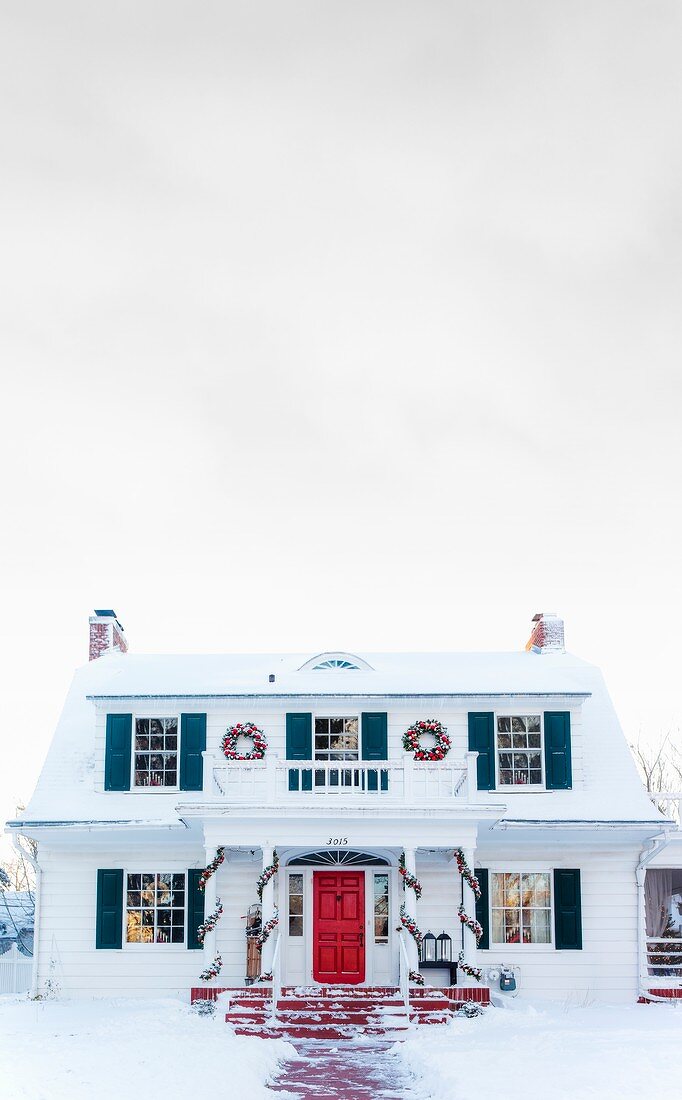 Weisses, amerikanisches Landhaus im Schnee mit farbigen Fensterläden und weihnachtlicher Deko