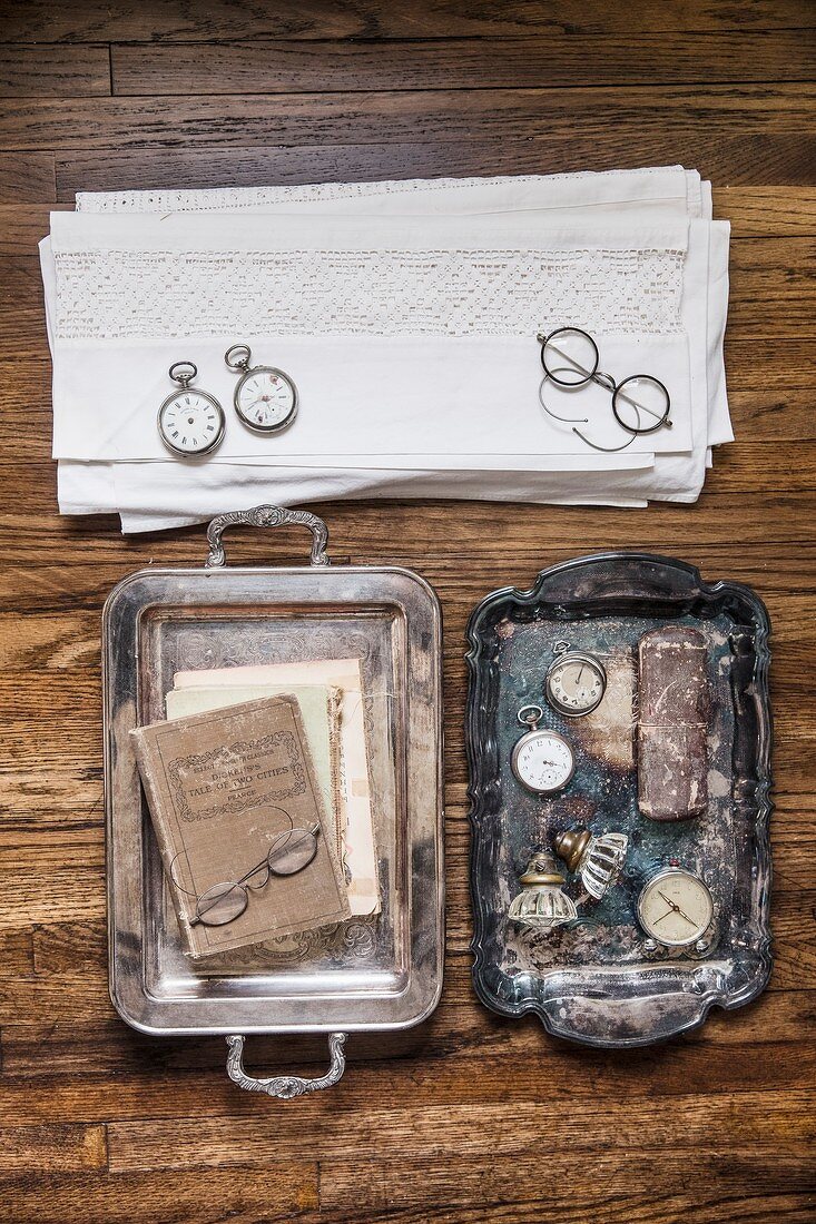 Antike Tabletts mit Taschenuhren, nostalgisches Brillengestell und Stapel Spitzendeckchen
