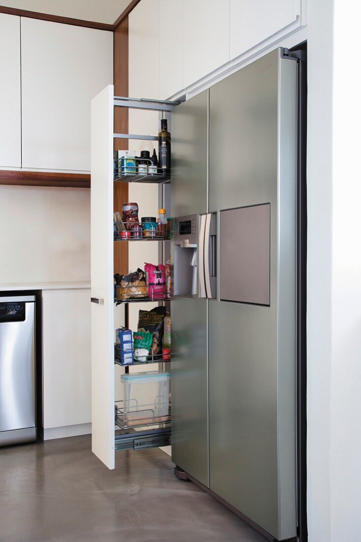 Open, sliding shelves next to stainless steel fridge-freezer in modern kitchen