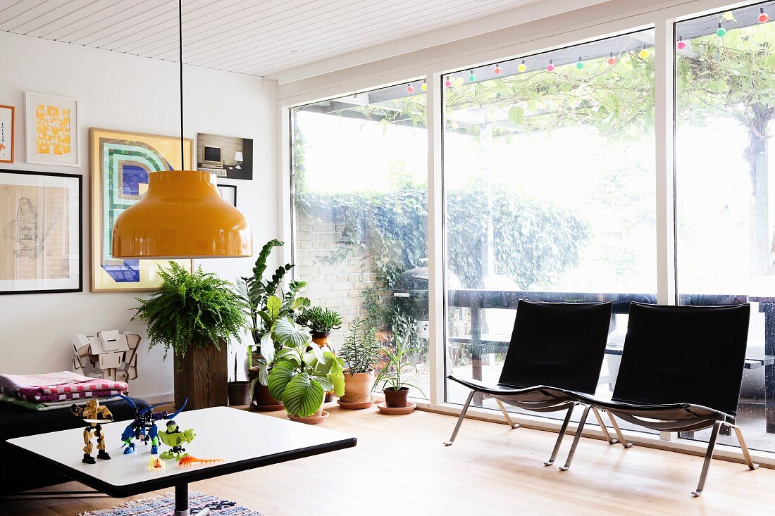 Schwarze Designersessel vor Terrassenfensterfront in Wohnbereich mit Retroflair und Zimmerpflanzen
