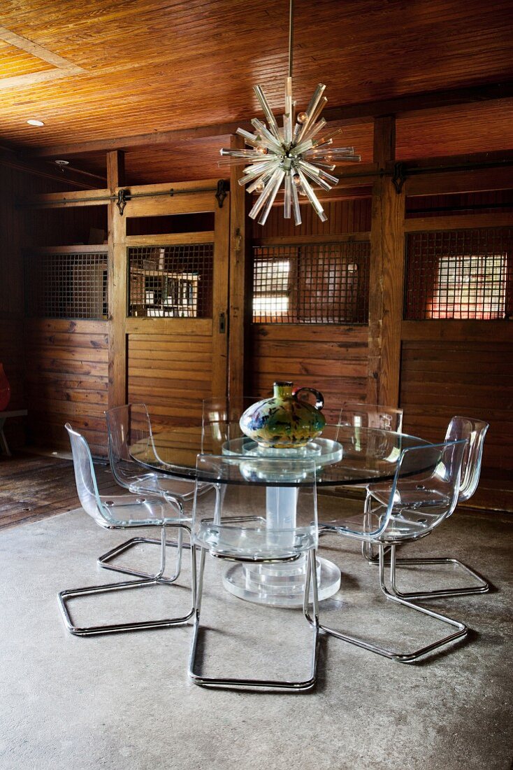Stühle aus Metall und Plexiglas um runden Glastisch in einem ehemaligen Stall