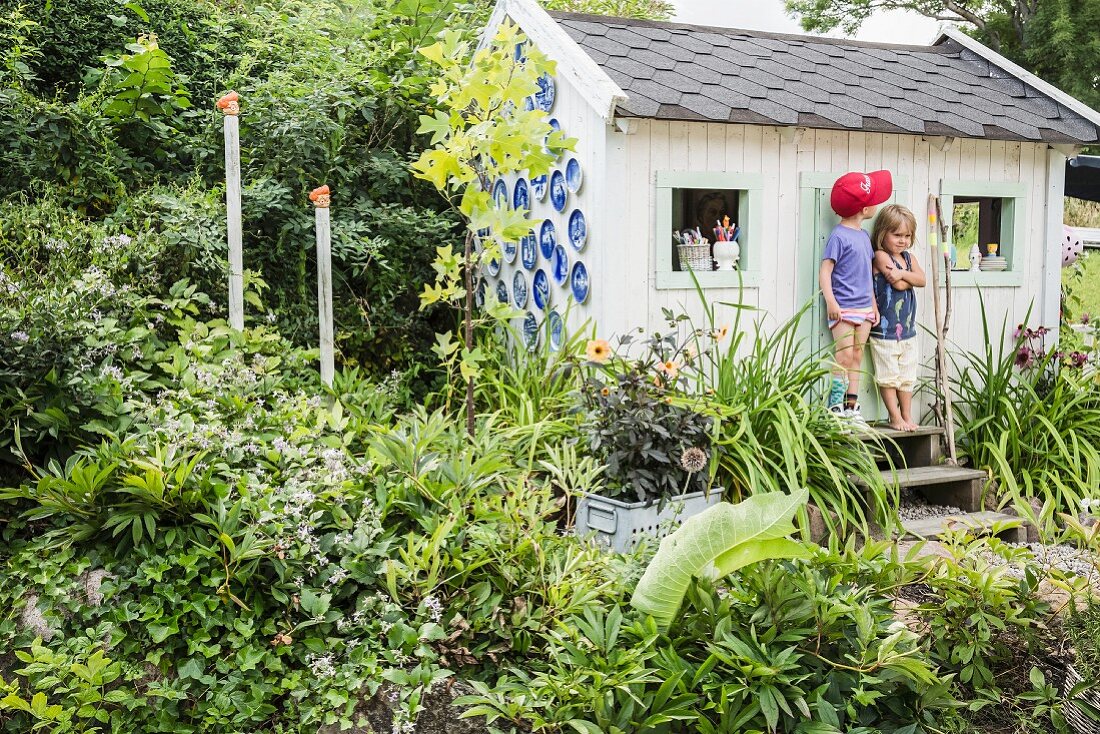 Two children outside play house in summery garden