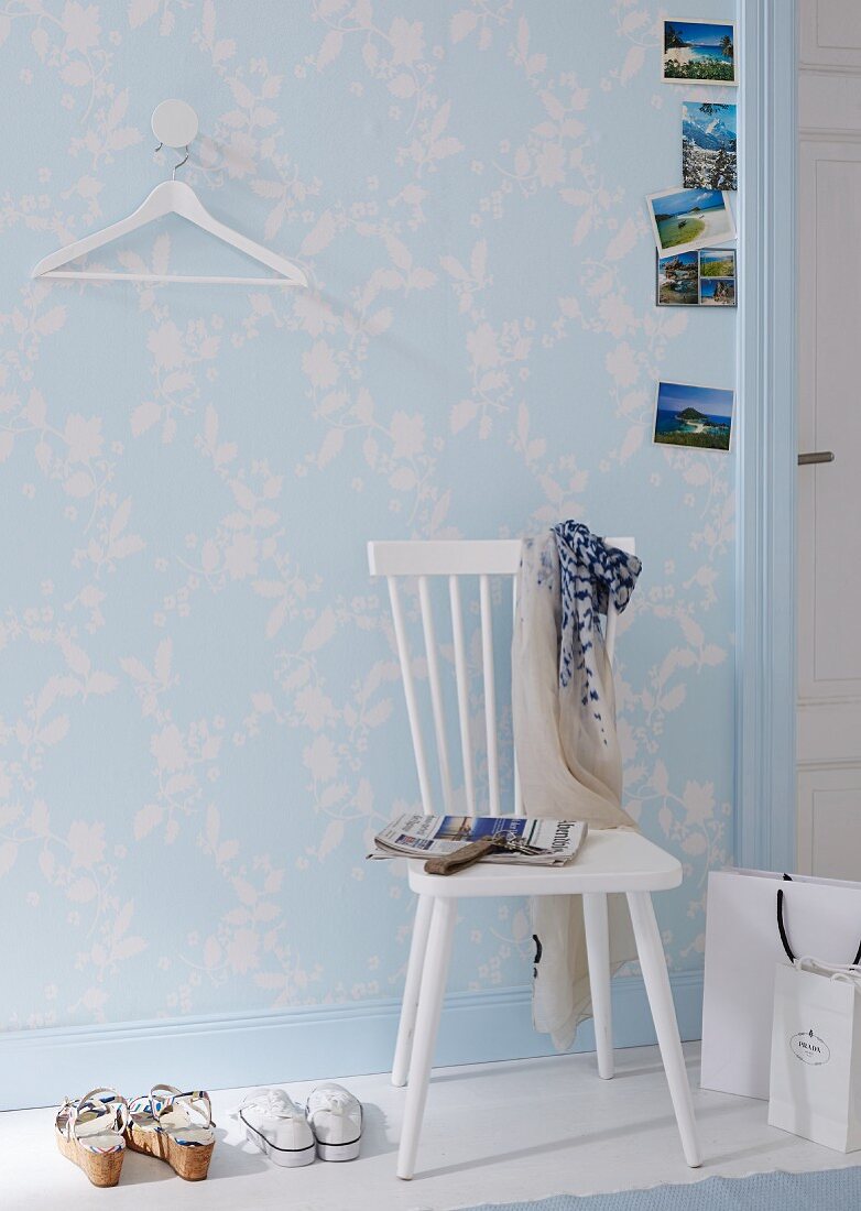 A white kitchen chair against a wall with pastel-blue and white floral-patterned wallpaper