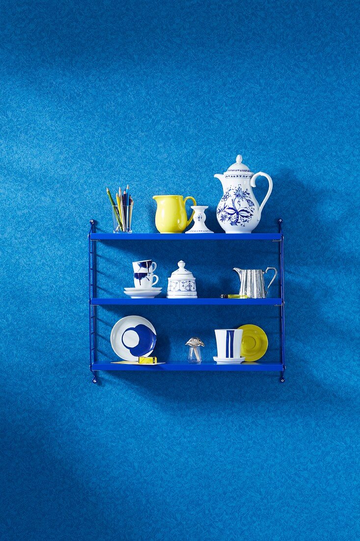 Blaues Stringregal mit Geschirr, an tapezierter Wand mit Faux-Unis Muster in Blau