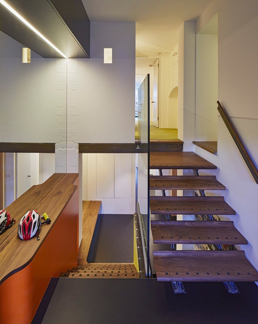 Designertreppe mit Glasbrüstung und Edelholzstufen, Blick in Flurbereich und auf orangefarbene Mauerbrüstung mit Holzablage