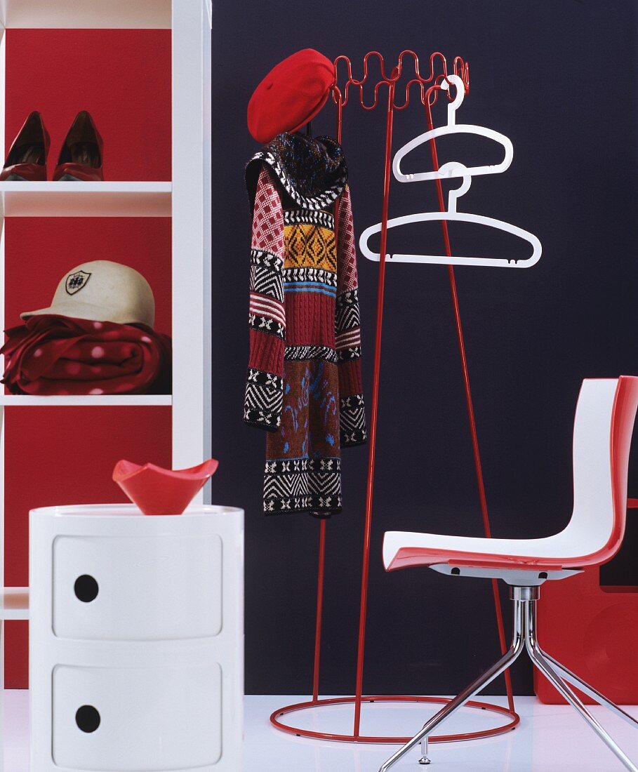 Garderobenmöbel in rot-weiß mit Kleiderbügel und Garderobenständer vor dunkler Wand und Retro-Flair