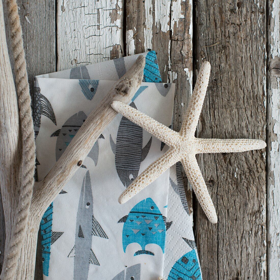 Dried starfish, driftwood & napkin with maritime print on weathered wooden surface