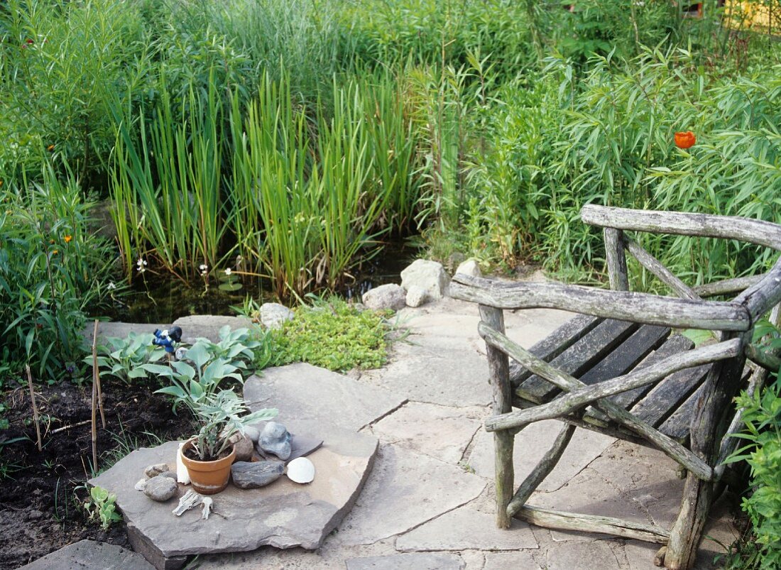 Sitzplatz im Garten mit Steinplatten an kleiner sumpfiger Teichanlage