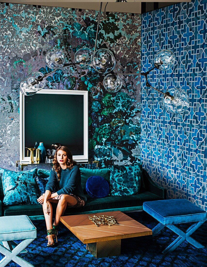Mustermix in Blautönen: Junge Frau auf einem Sofa im Wohnzimmer mit verschieden tapezierten Wänden