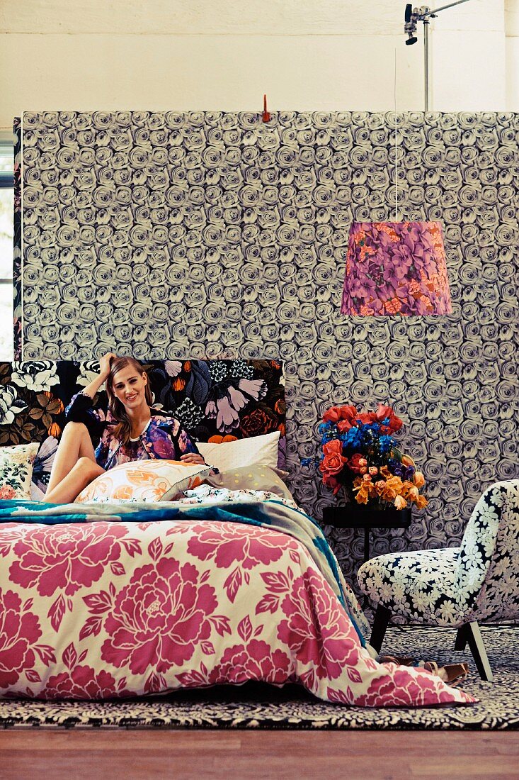Junge Frau sitzt auf dem Bett im Zimmer mit verschiedenen Mustern
