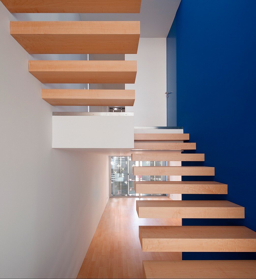 Minimalistische Treppe mit auskragenden Holz Trittstufen, eine Wandseite königsblau getönt
