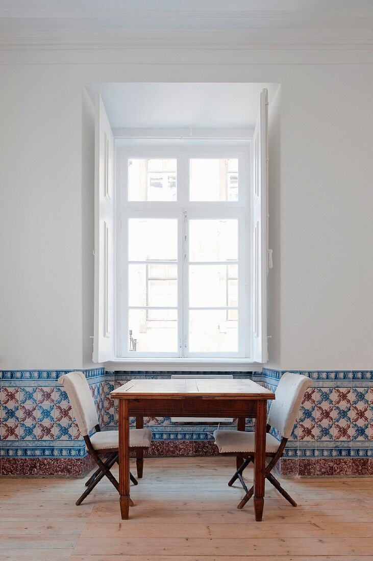 Table and upholstered chairs below window; dado strip covered with hand-painted tiles