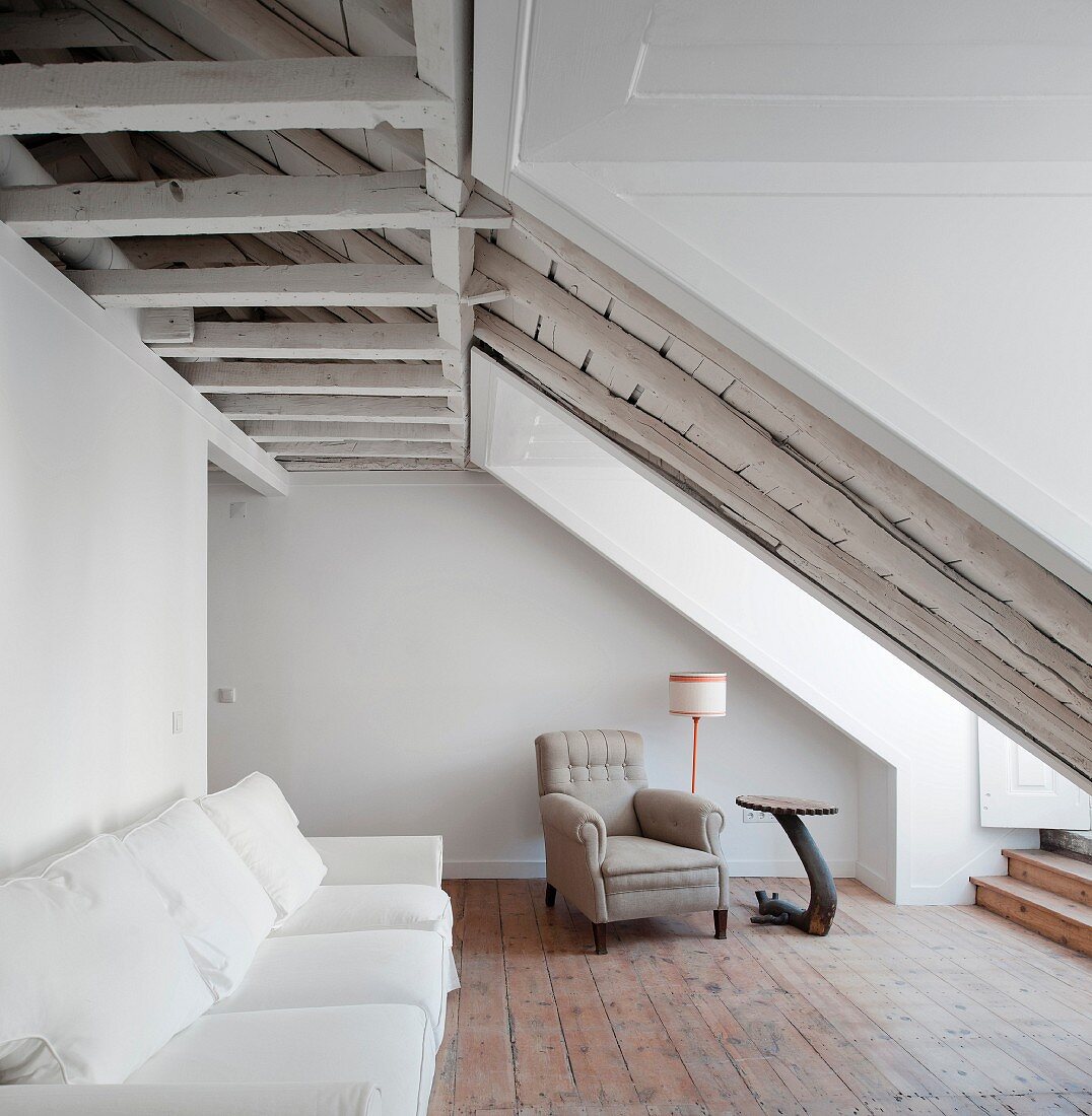 Weisses Sofa an Wand, im Hintergrund traditioneller Sessel, in ausgebautem Dachgeschoss mit rustikalem Flair