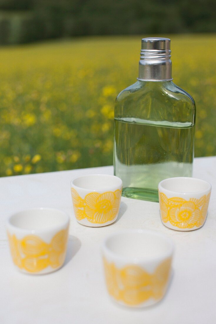 White beakers with yellow, retro pattern and flask of spirits on white surface outdoors