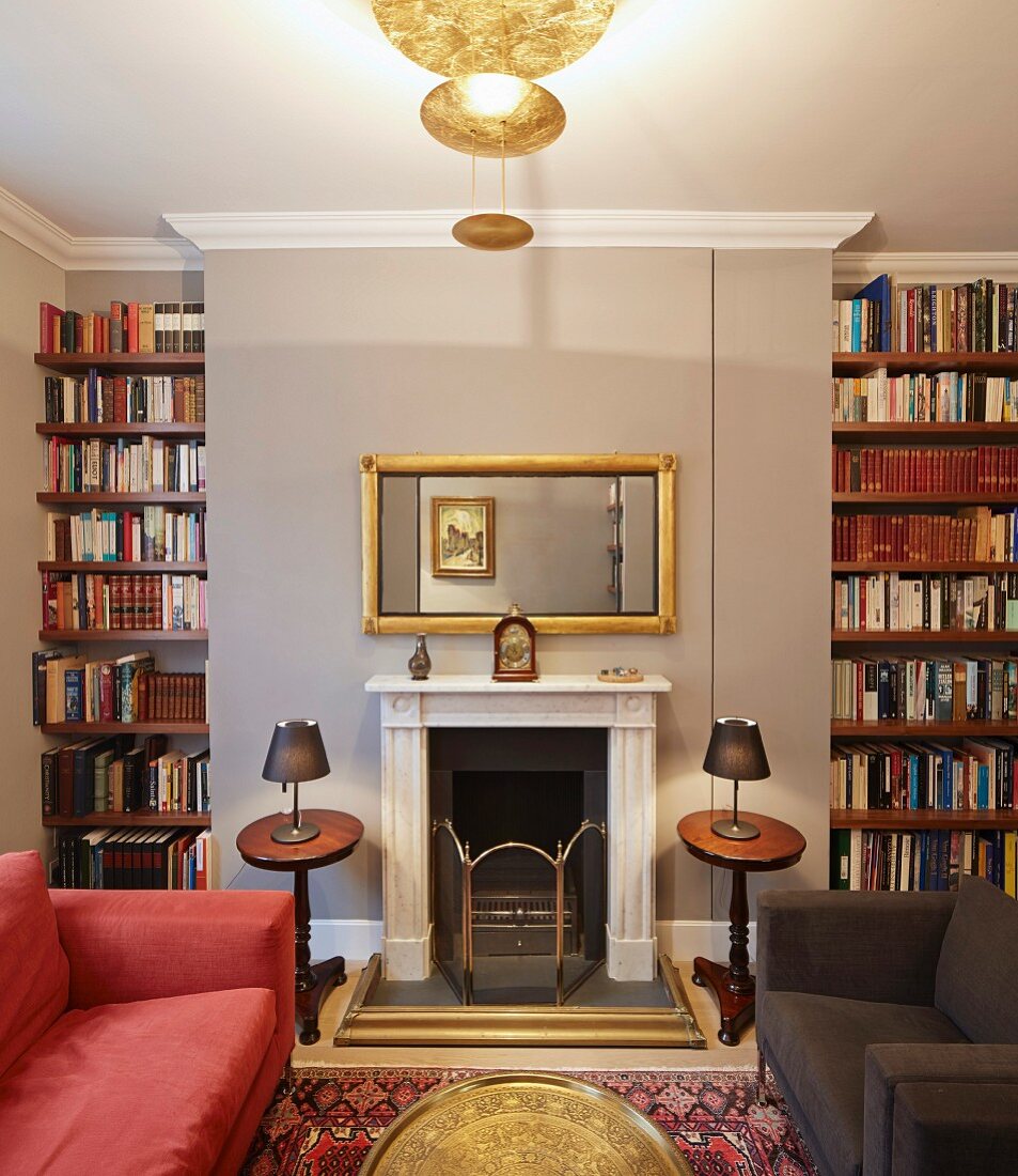 Moderne Sitzmöbel in rot und dunkelbraun vor offenem Kamin, goldfarbene Designer-Deckenleuchte in elegantem Wohnzimmer mit traditionellem Flair