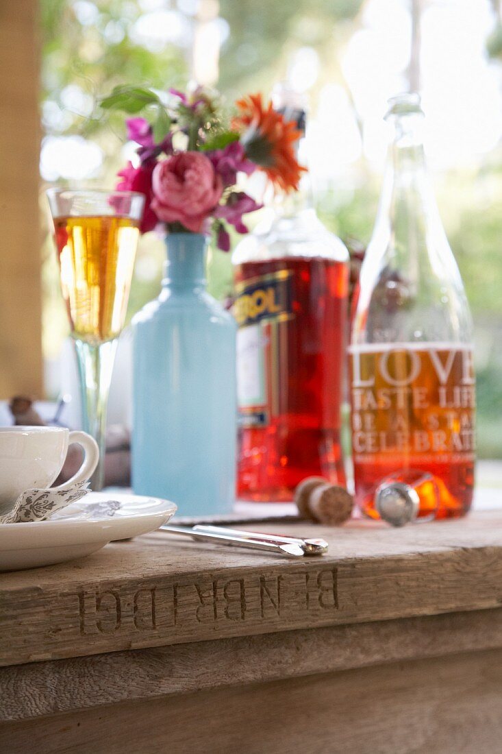 Hellblau bemalte Flaschenvase mit Herbstblumenstrauss und Getränke auf rustikalem Holztisch