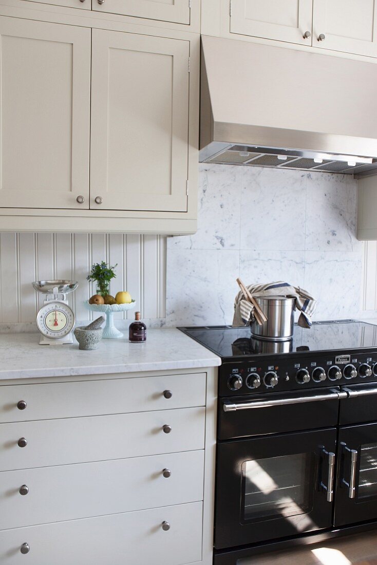 weiße Küche mit schwarzem Küchenherd, oberhalb Hängeschrank mit integriertem Dunstabzug
