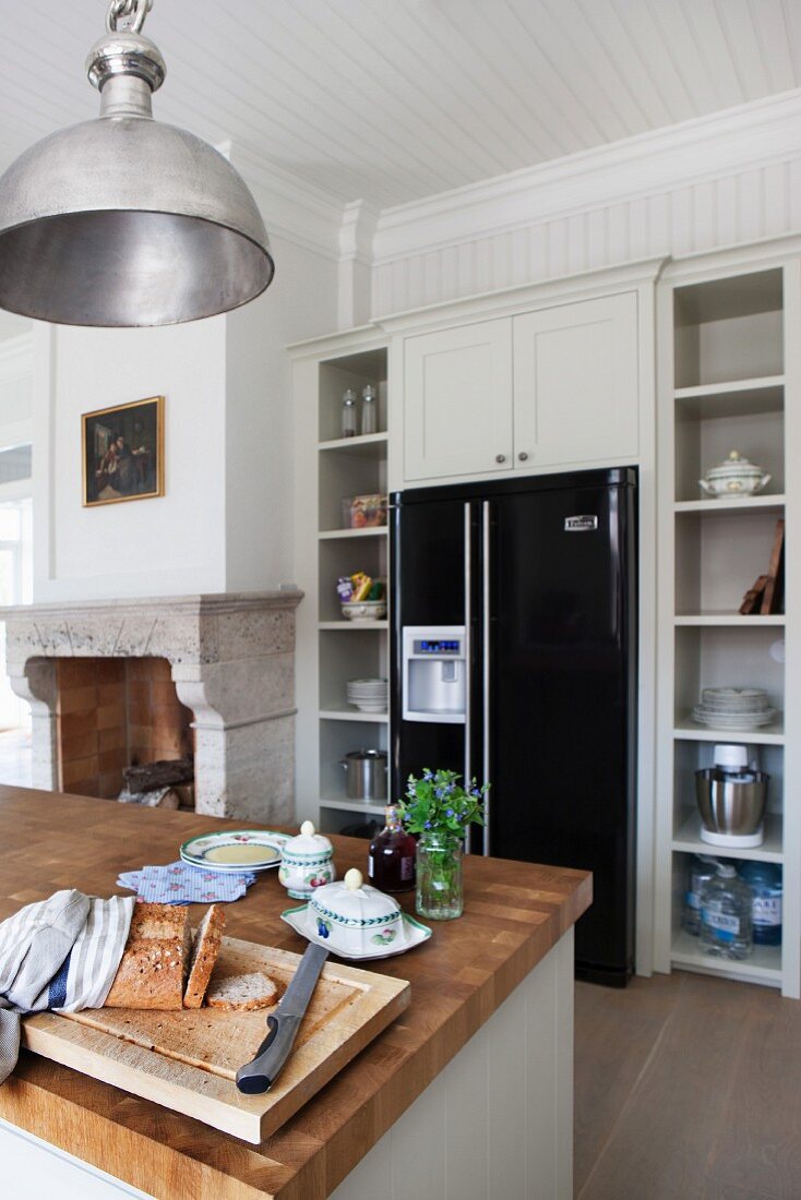 Kücheninsel mit Holz Arbeitsplatte, gegenüber moderne, schwarze Kühlschrankkombination integriert in Einbauküche im Landhausstil