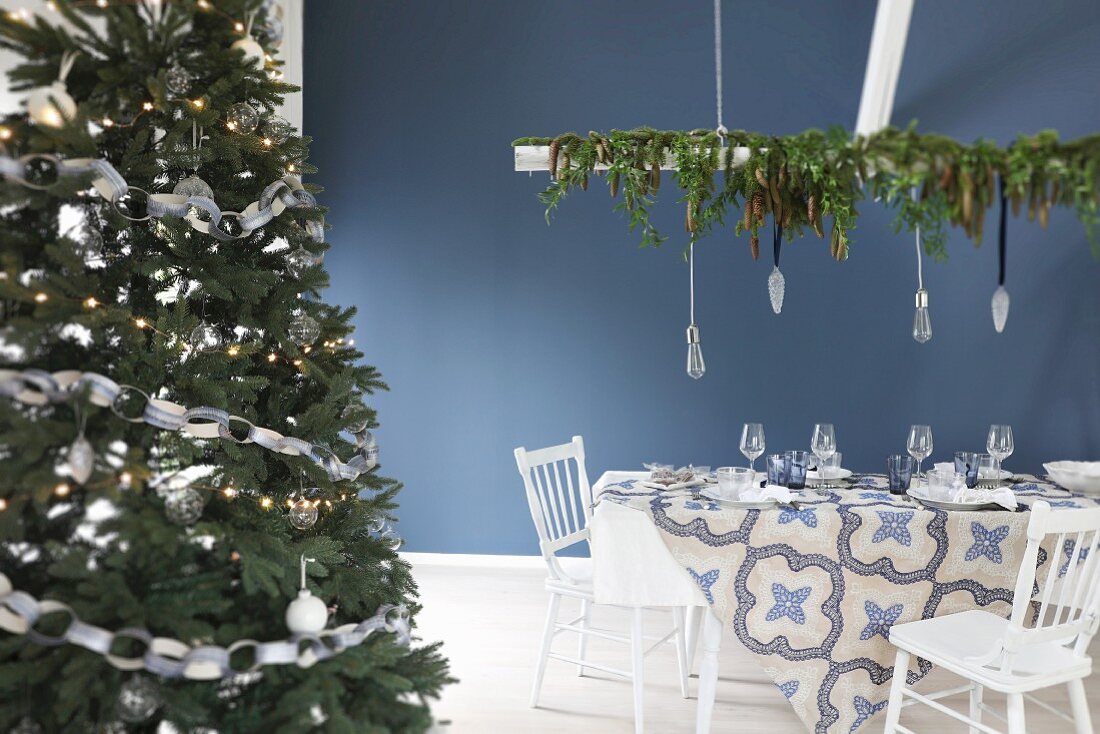 Gedeckter Weihnachtstisch in Blau-Weiß neben geschmücktem Weihnachtsbaum