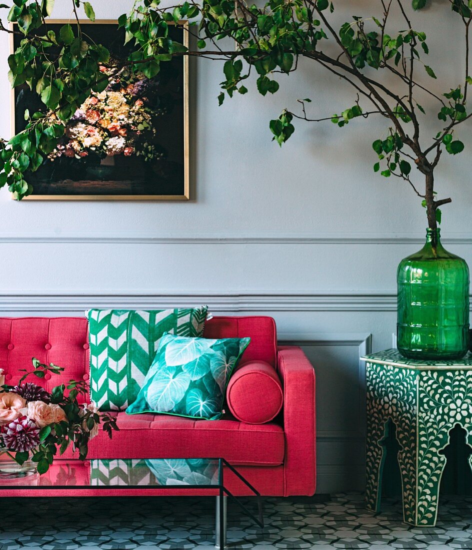 Pinkfarbenes Sofas mit Kissen, neben Blätterzweig in Glasvase