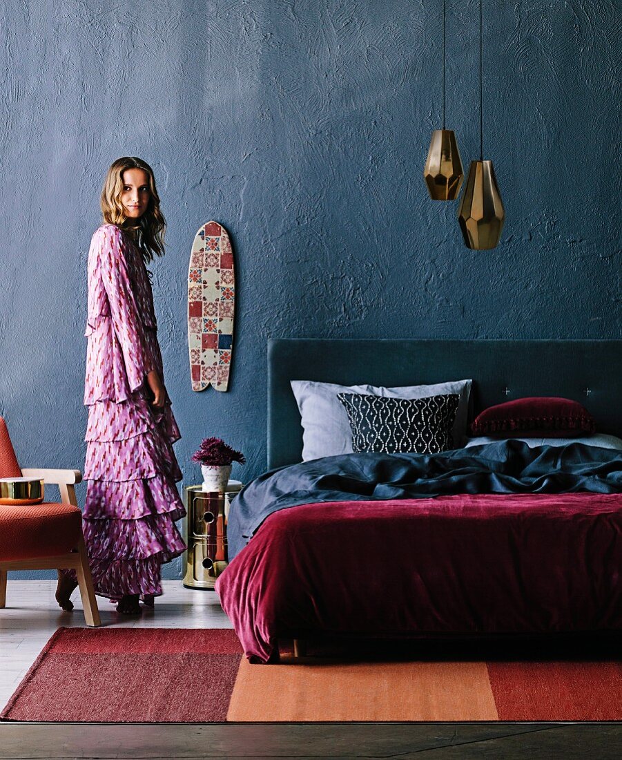 Schlafraum mit Doppelbett vor grauer Wand unter Messing Pendelleuchten, Frau mit Bohemian-Flair