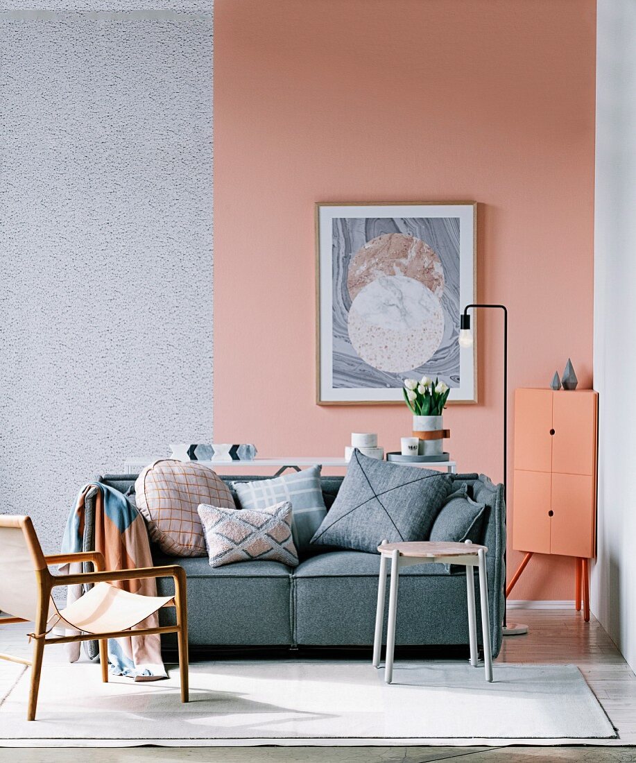 Sitzmöbel im Retrostil vor grauem Sofa mit Kissen, Wand mit gemusterter und unifarbener Wandfläche