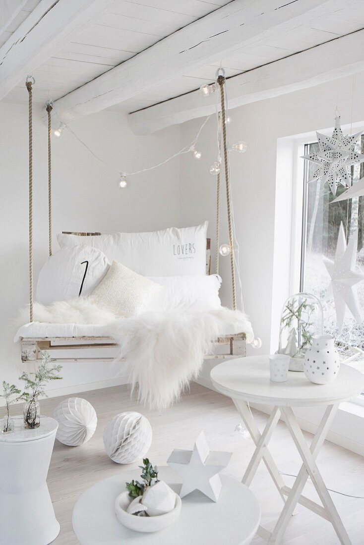 DIY swing made from pallet with white sheepskin rug and cushions in white room with Christmas decorations