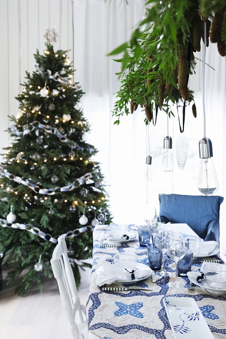 Gedeckter Weihnachtstisch in Blau-Weiß vor einem Weihnachtsbaum